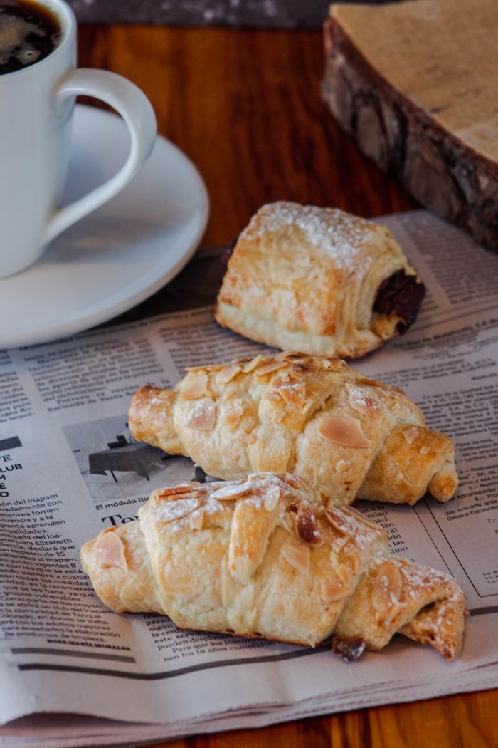 A cozy breakfast setting with croissants, chocolate pastry and coffee on a wooden table.